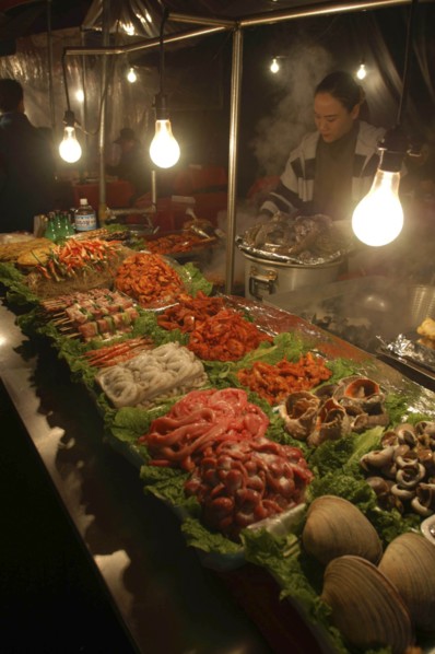 KOREA, Seoul, "Namdaemun Market on a cold December night with a woman cooking behind trays of fresh