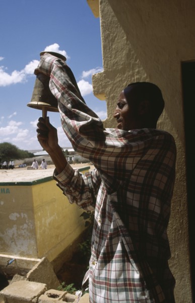 SOMALILAND, Hargeisa, Gacmodhere primary School.  Male teacher ringing school bell.