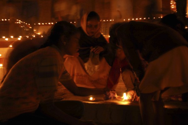INDIA, Uttar Pradesh, Varanasi, Deep Diwali Festival with young girls lighting oil lamps on steps
