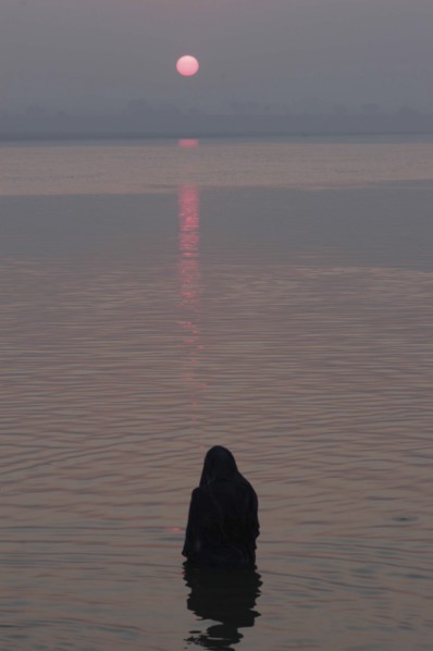 INDIA, Uttar Pradesh, Varanasi, Asi Ghat. A Hindu man baths in the Ganges River with the early