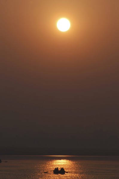 INDIA, Uttar Pradesh, Varanasi, Ganges River at dawn with rowing boat silhouetted against warm