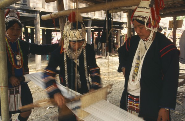 THAILAND, Chiang Mai, Akha woman weaving cloth on an Akha loom as other women look on