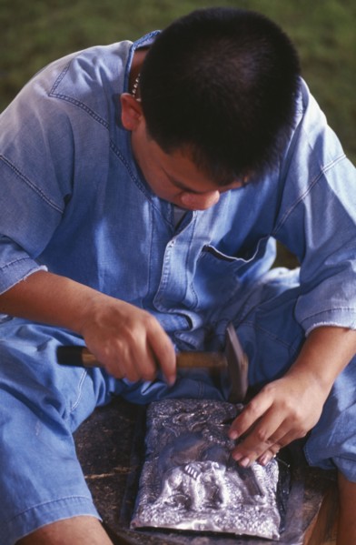 THAILAND, Chiang Mai, Wat Sri Suphan, Silversmith making repousse picture of elephants