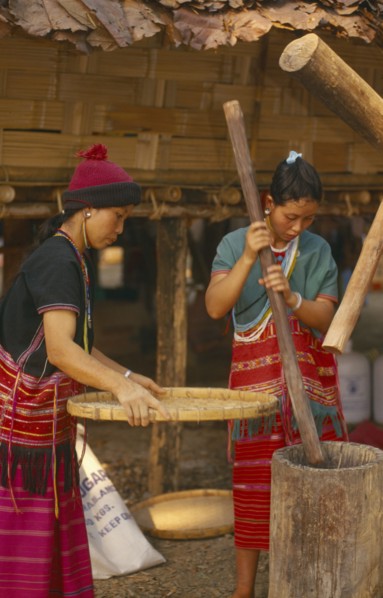 THAILAND, Chiang Mai, Sgaw Karen woman pounding rice by hand while another sifts with a large