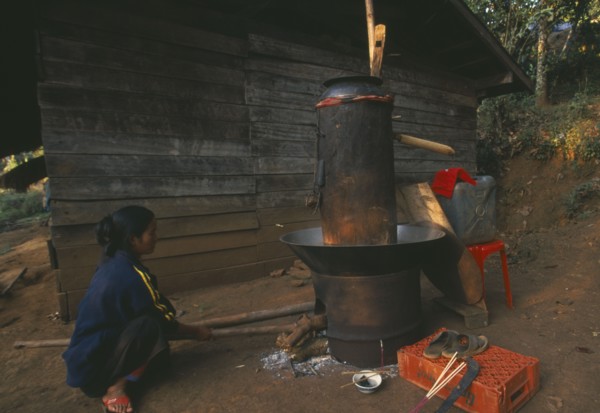 THAILAND, Chiang Rai Province, Doi Lan, Lisu woman stoking fire of her still for making corn