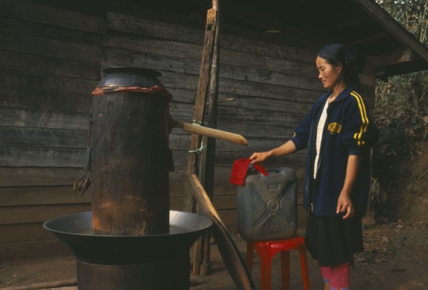 THAILAND, Chiang Rai Province, Doi Lan, Lisu woman checking cloth filter on the spout of her still
