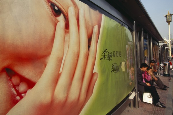 CHINA, Beijing, People waiting at bus stop south of Tiananmen Square with advertising hoarding
