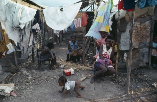 HAITI, People, Group of laughing women and children in shanty village sitting outside underneath
