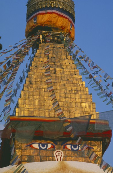 NEPAL, Kathmandu, Bodnath Stupa, Detail of spire of stupa with painted eyes and hung with prayer