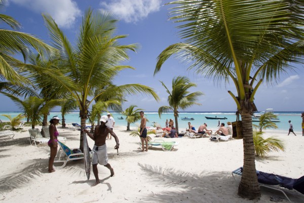 WEST INDIES, Barbados, Christ Church, Fisherman carrying gutted King Fish past tourists and coconut