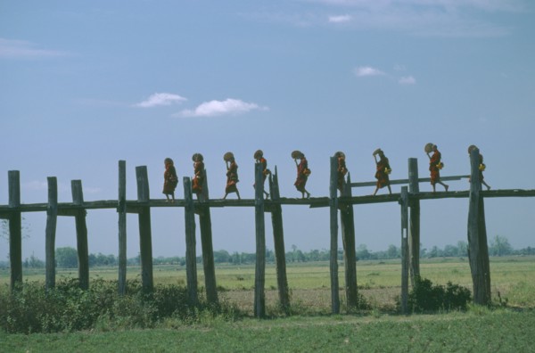 MYANMAR, People, Line of monks with fans crossing wooden bridge raised high above agricultural land