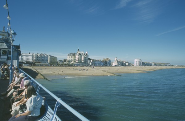 ENGLAND, East Sussex, Eastbourne, View from pier with people sat on seats towards beachfront.