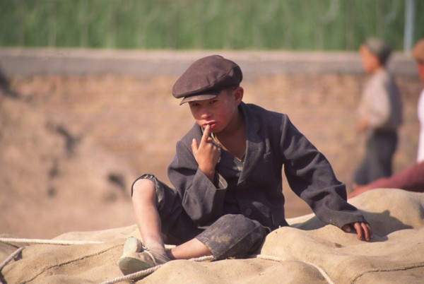 CHINA, Xinjiang Province, Kashgar,  Tajik boy sat on sacks