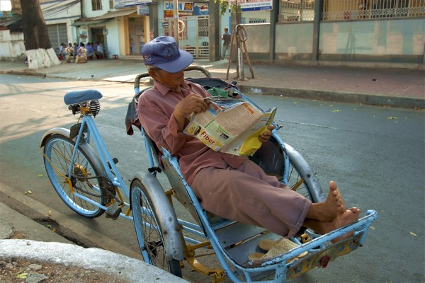 VIETNAM, South, Ho Chi Minh City, A Cyclo driver reading a magazine taking a break