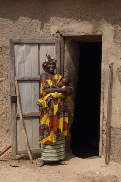 MALI, People, Portrait of Malian mother and breastfeeding baby standing outside open doorway of mud