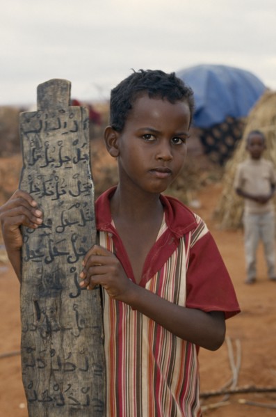 KENYA, Mandera, Somali refugee camp run by UNHCR.  Young boy attending Koranic school holding piece