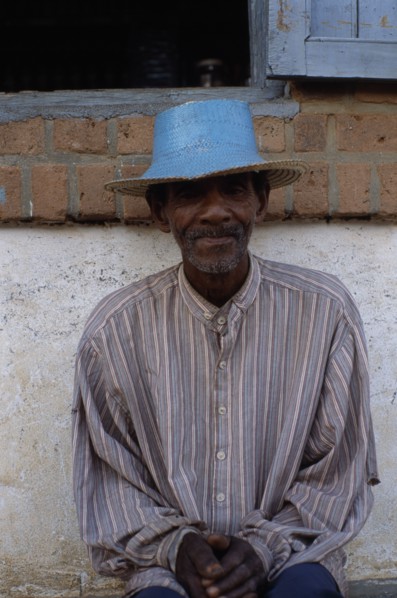 MADAGASCAR, Ihosy, Portrait of an elderly man sitting against a wall wearing a blue straw hat