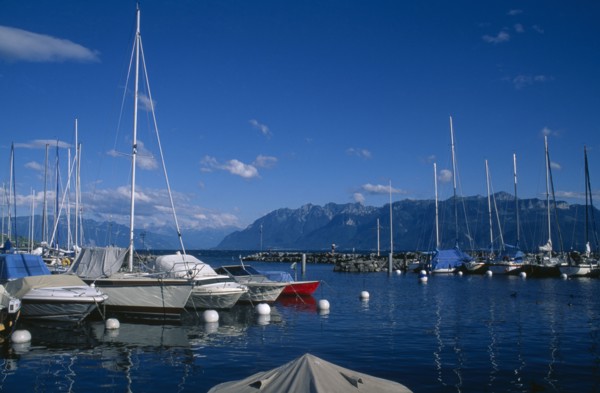 SWITZERLAND, Vaud, Lutry, Boats moored in marina with view across Lake Geneva beyond.