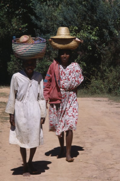 MADAGASCAR, People, Women, Near Ambositra. Two barefooted women walking up a dirt track carrying