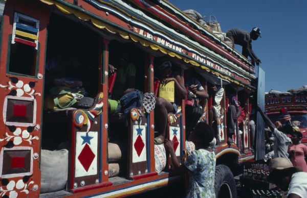 HAITI, Transport, Colourfully painted bus with people loading goods onto the roof