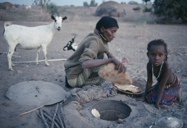 ETHIOPIA, North East, Afar tribeswoman baking bread in ground with child sitting beside her.