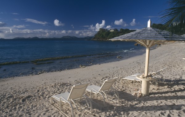 GRENADINES, Mustique, Endeavour Bay. Empty sun loungers on sandy beach with Bequia Island seen from