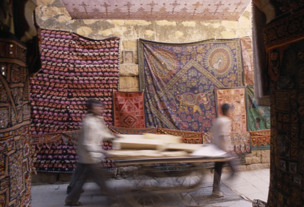 INDIA, Rajasthan, Jaisalmer, Jaisalmer Fort. Two men pushing a cart through a narrow street with