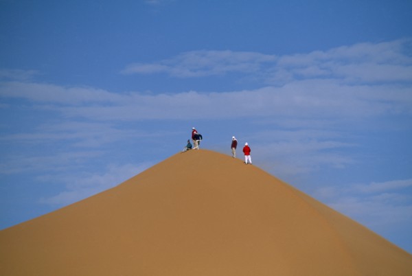LIBYA, Sahara Desert, Tourists standing on top of Saharan sand dune.