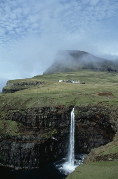 DENMARK, Faeroe Islands, River Gazadalla, Waterfall and rocky coastline with houses built on green
