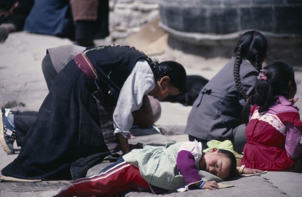 TIBET, Lhasa, Pilgrims at Jokhang Monastery.  Kneeling woman and prostrate child on ground in front