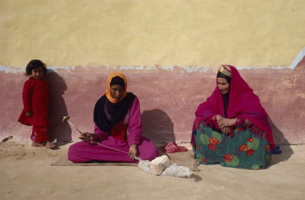EGYPT, Western Desert, Bedouin, "Women and child in colourful dress spinning wool, sitting against