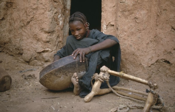 MAURITANIA, Oualata, Young girl cleaning bowl after meal with frame for carrying goods by donkey on