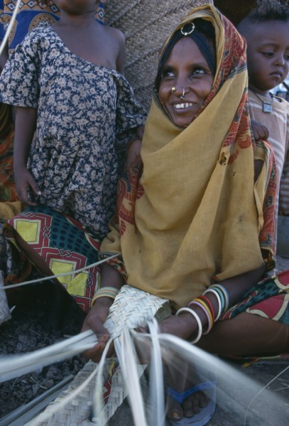 ERITREA, Barentu, Woman making mats with children standing behind her