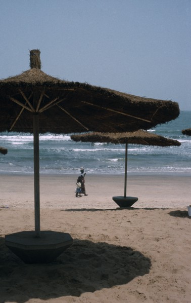 GAMBIA, Landscape , Beach, Beach with straw sun shades and a woman with children walking along the