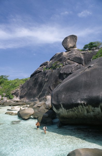THAILAND, Koh Similan  , Sail Rock, A couple walking in the water at the base of the large rocks.