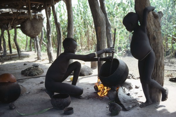 SUDAN, Tribal People, Dinka children cooking over open fire beneath house raised above ground level