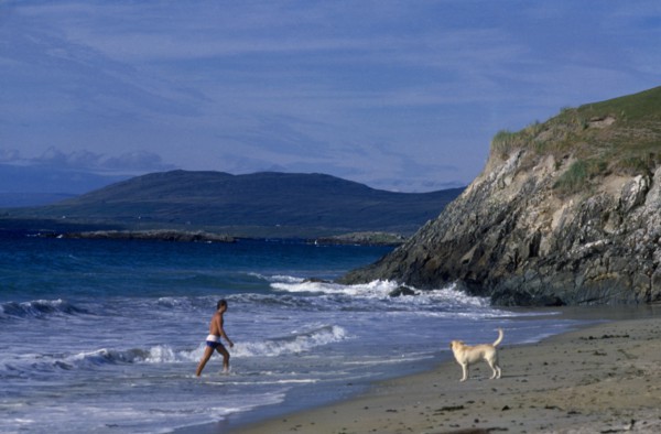 IRELAND, County Galway, Galway, Beach with man walking out of surf towards a dog on the sand
