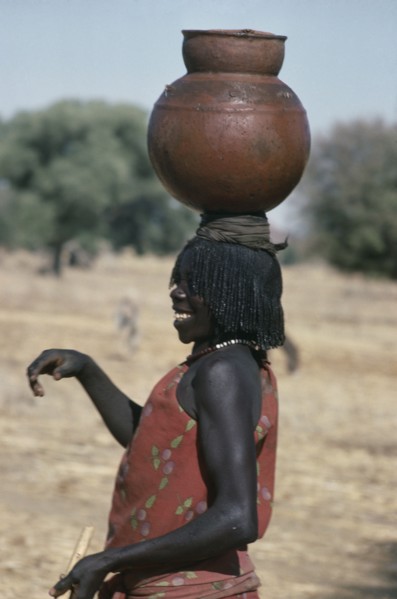 SUDAN, Habila Settlement, Laughing Chadian refugee woman carrying water pot on her head.