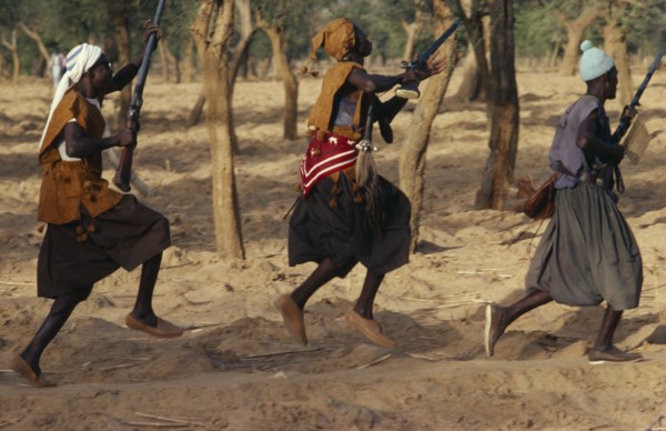 MALI, Ceremony, Dogon funeral dance.  Dancers carrying rifles leaping in line.