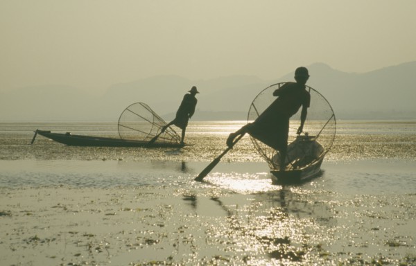 MYANMAR, Shan State, Inle Lake, Silhouettes of two Intha fishermen with Sun’s reflection on water.
