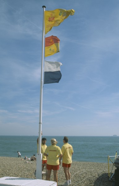 ENGLAND, Hampshire, Portsmouth, Lifeguards on beach under flag pole.