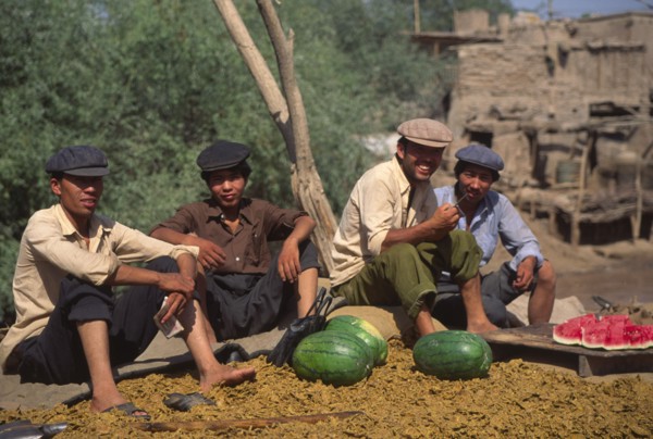 CHINA, Xinjiang Province, Kashgar, Group of Tajik men sat on ground eating water melon