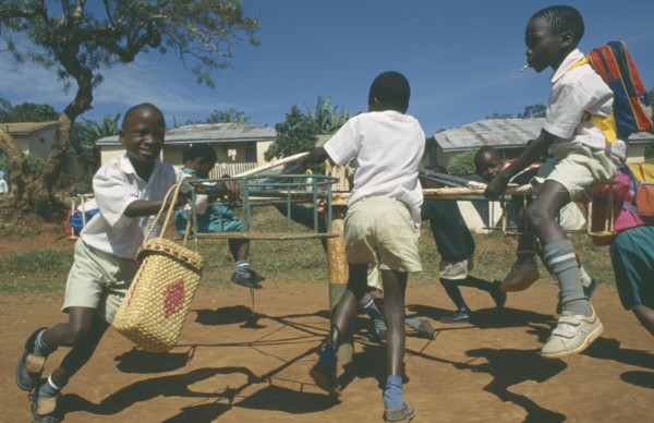 UGANDA, Mengo, Primary school children playing on roundabout. Young boy smoking cigarette.