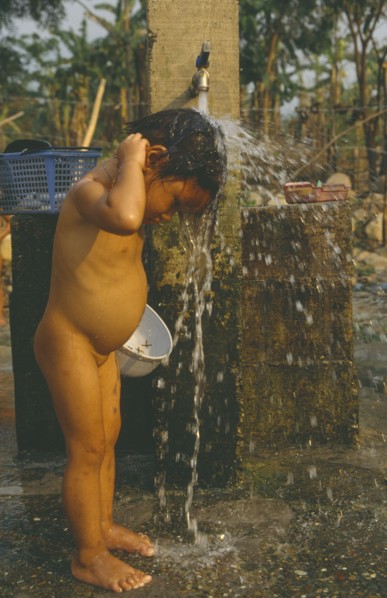 LAOS, Hygiene, Washing, Young Hmong girl washing under stand pipe in Hmong returnee villages for
