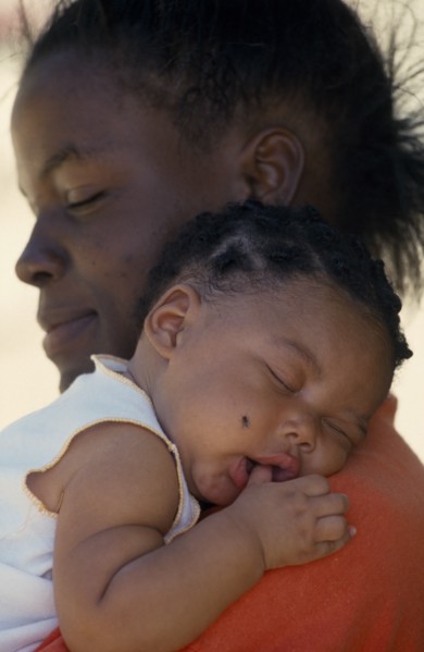 WEST INDIES, St Lucia, Portrait of young mother holding baby girl asleep on her shoulder with thumb