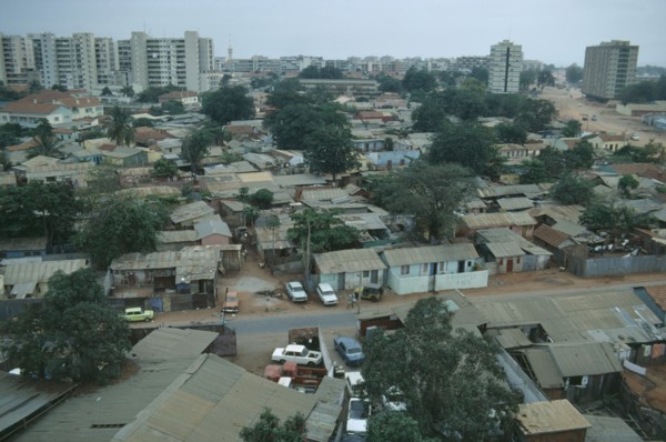 ANGOLA, Luanda, Cars parked next to houses along a road with high rise apartment blocks in the