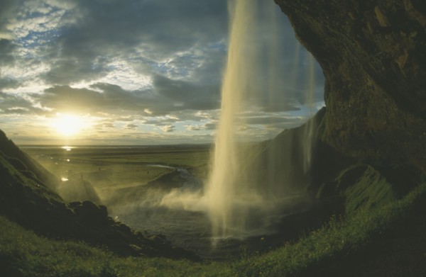 ICELAND, Seljalandfoss, View from behind waterfall in low golden sunlight through drifting cloud.