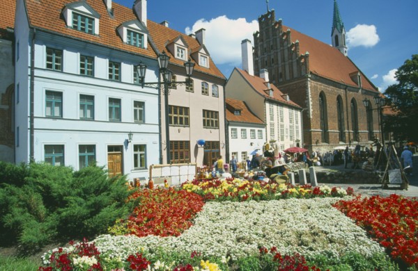 LATVIA, Riga, Church of St John beside town housing with colourful flowerbeds in the foreground on