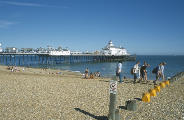 ENGLAND, East Sussex, Eastbourne, View across shingle beach towards pier with a group of people