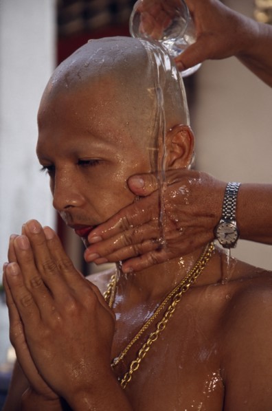 THAILAND, Bangkok, Novice monk having water poured over newly shaved head during ordination